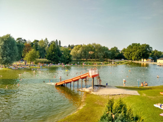 Eine Rutsche führt in das Naturbad Mockritz. Im und neben dem Wasser befinden sich Menschen